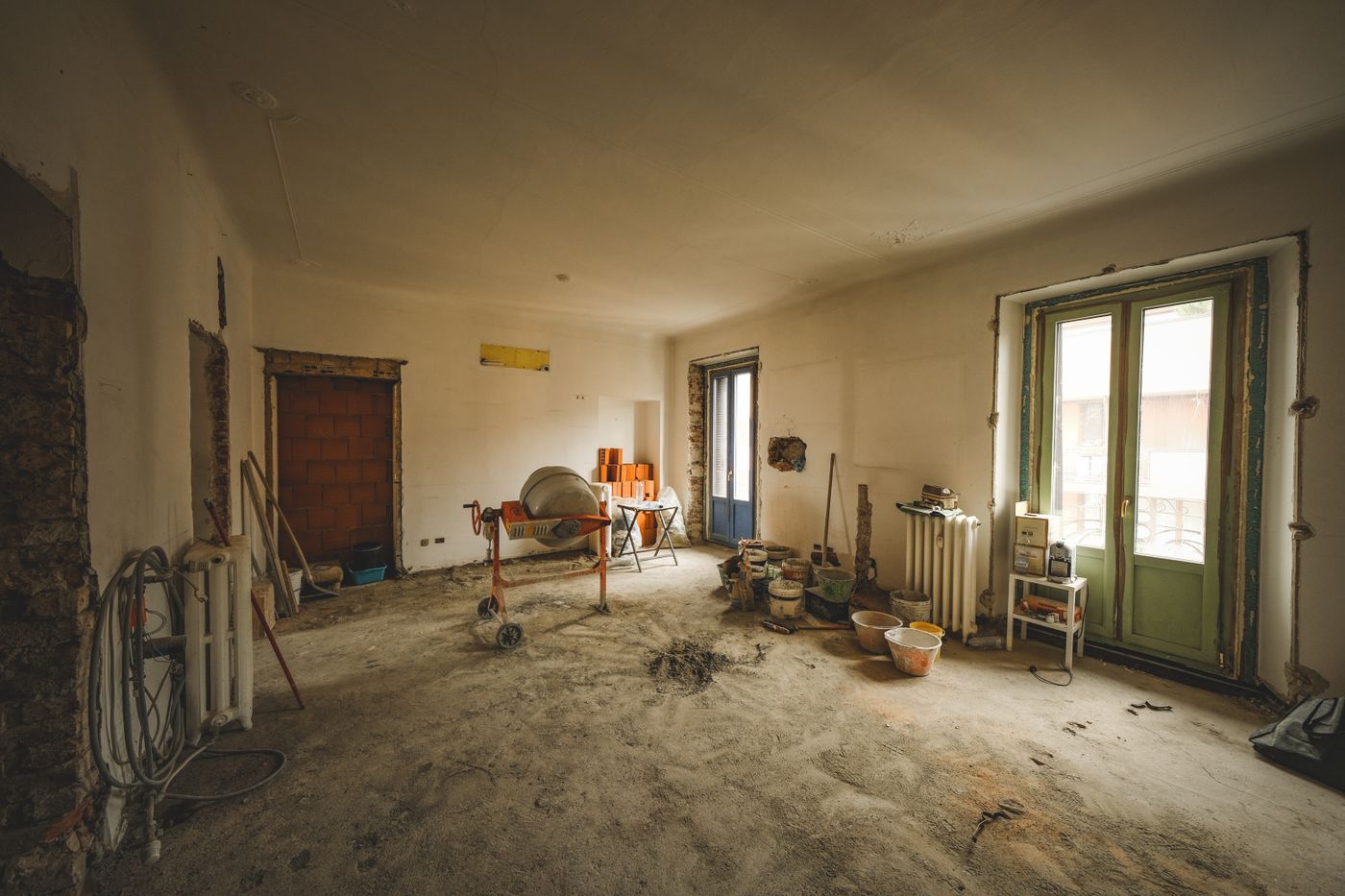 Místnost při rekonstrukci s míchačkou, kbelíky, radiátory a částečně odkrytými stěnami.