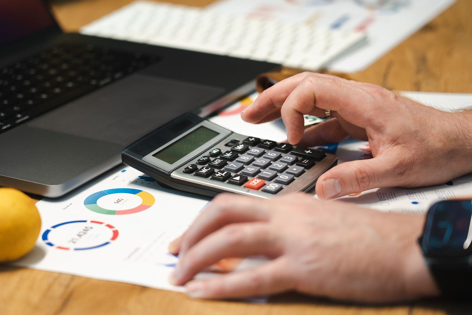 Une personne utilise une calculatrice devant un ordinateur et des documents chiffrés.