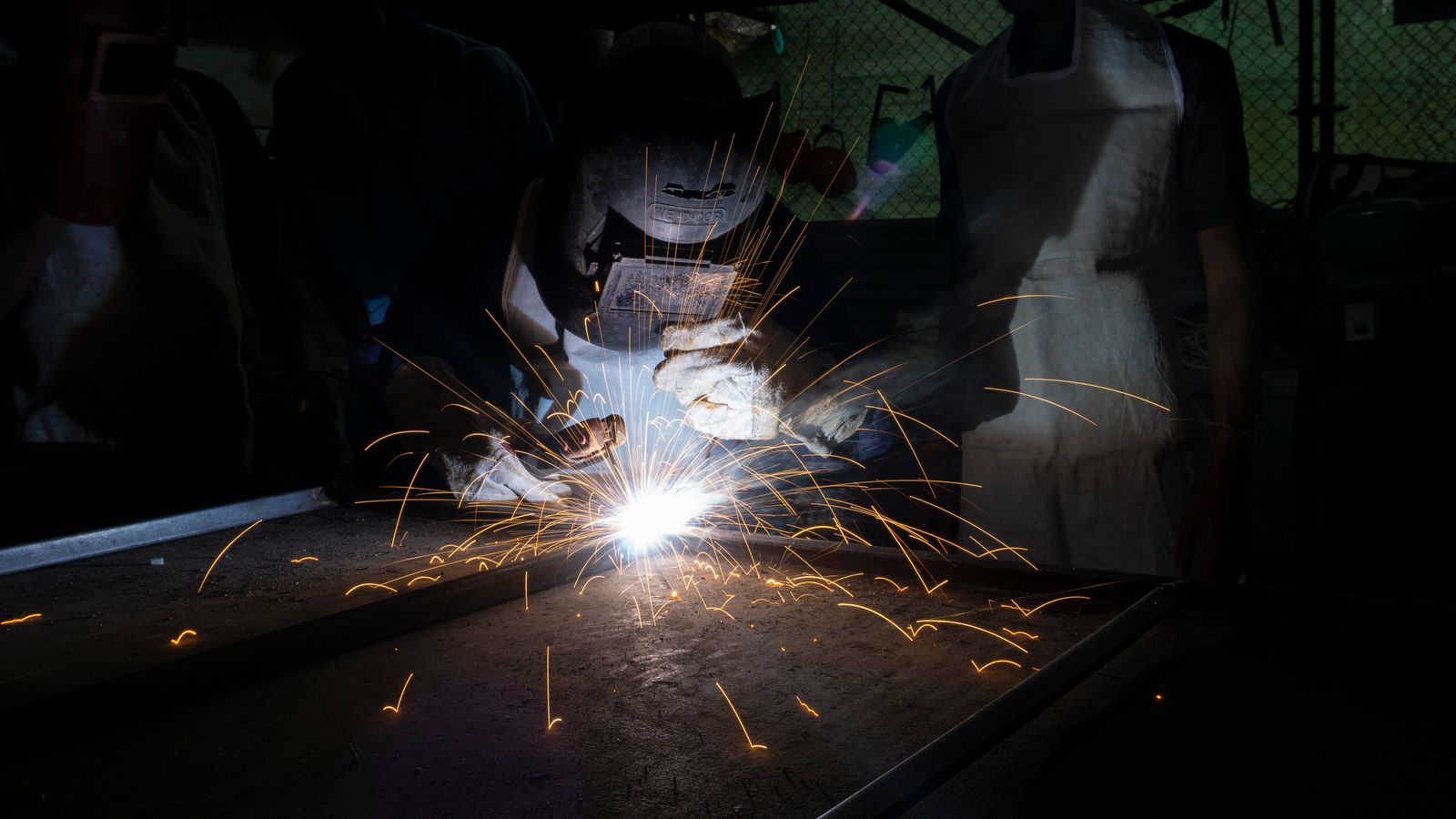 Saldatura di un pezzo metallico in officina, con scintille e visiera protettiva.