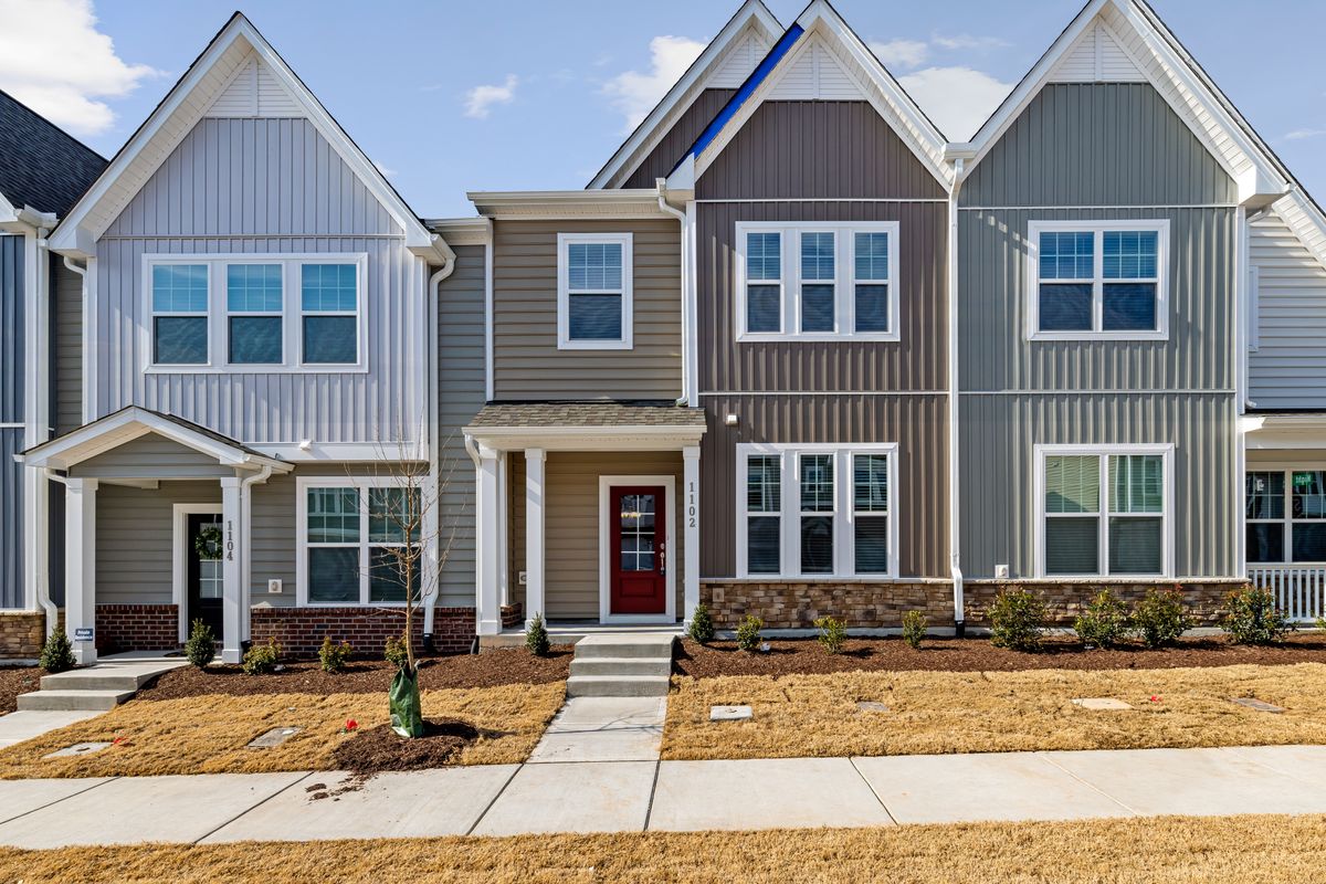 A row of two-storey terraced homes with light-coloured facades, lawns and front paths.