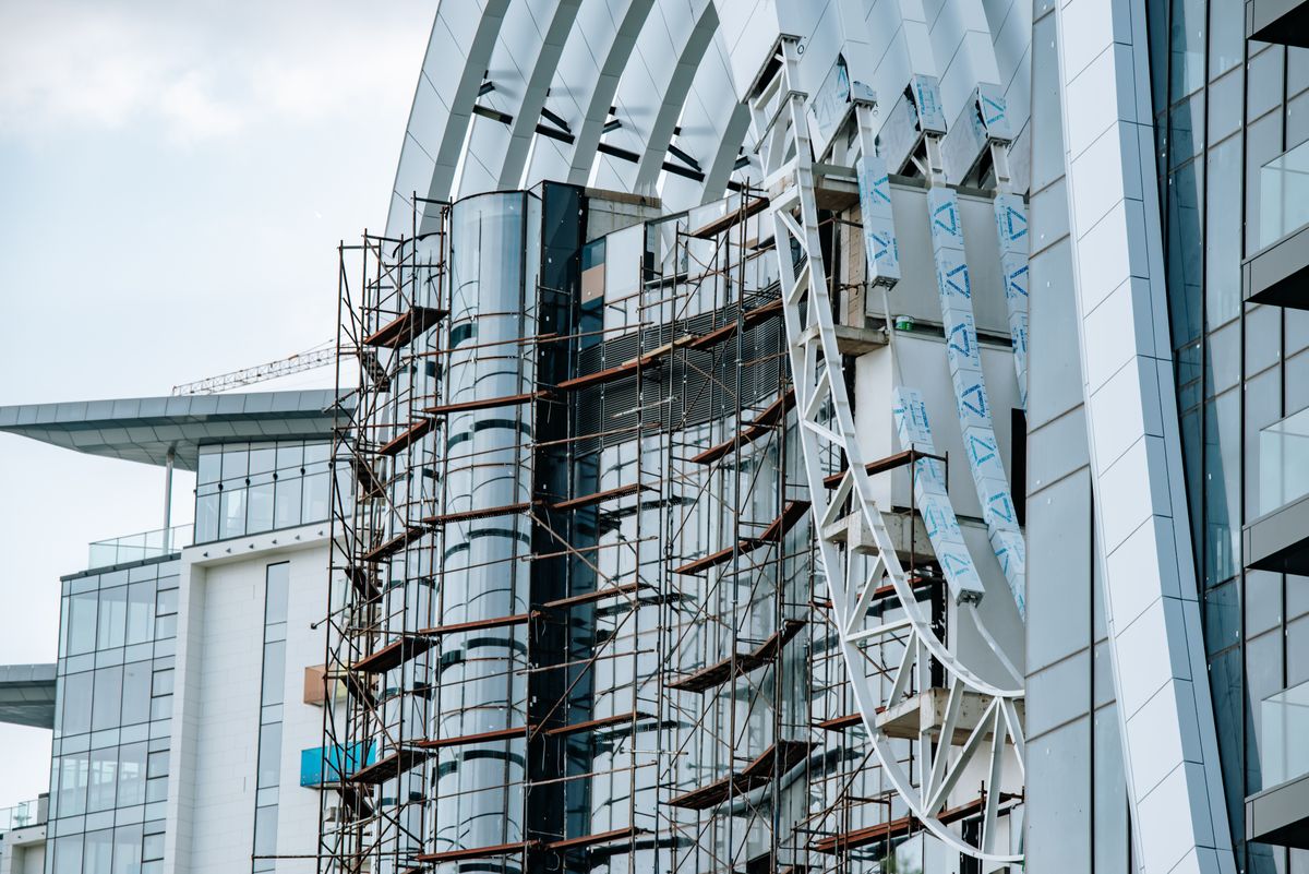 Scaffolding in front of a glazed facade with light-coloured panels during building work.