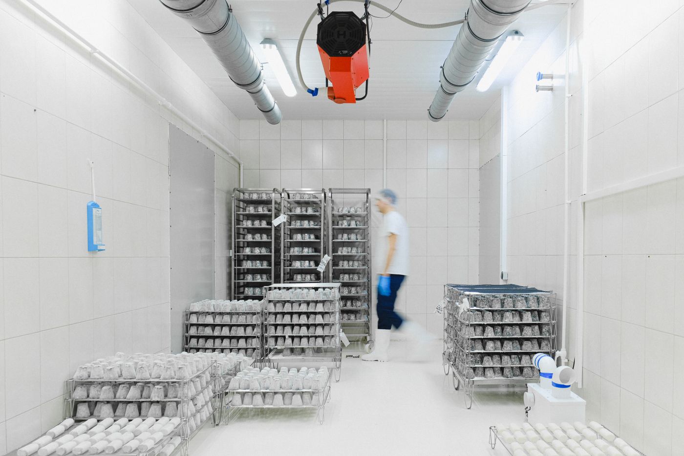 A food storage room with metal racks, overhead ducts and a person in the background.