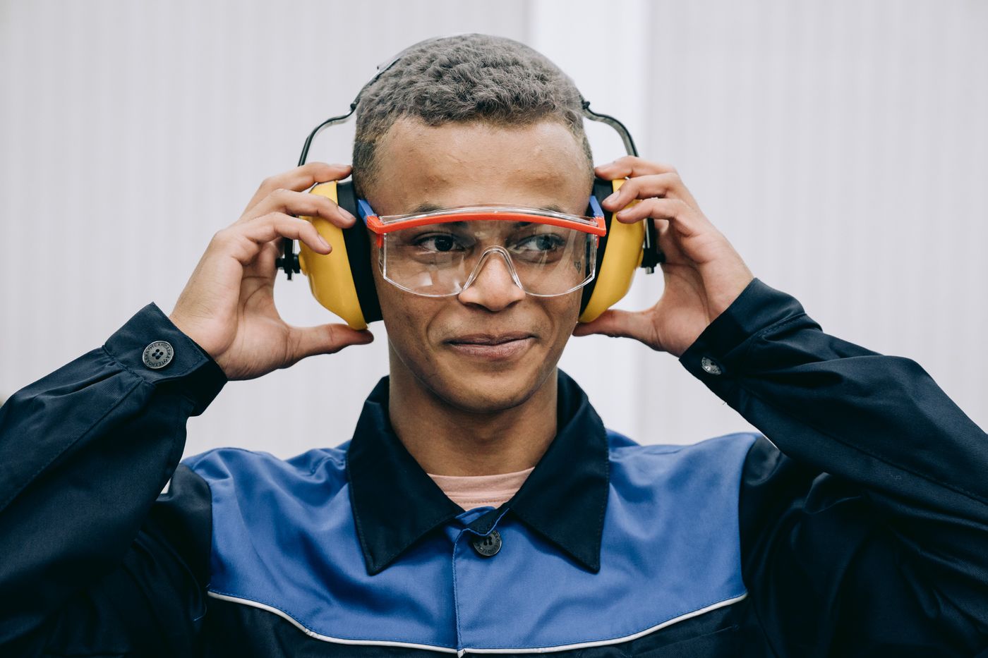 A person in workwear wearing safety glasses and adjusting yellow hearing protectors.