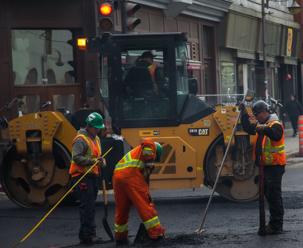 Workers and a road roller on a street construction site.