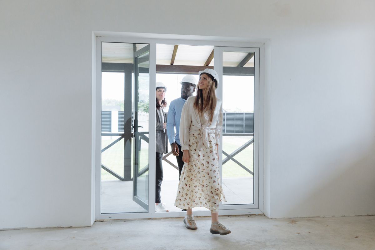 Three people wearing hard hats enter an unfinished building.