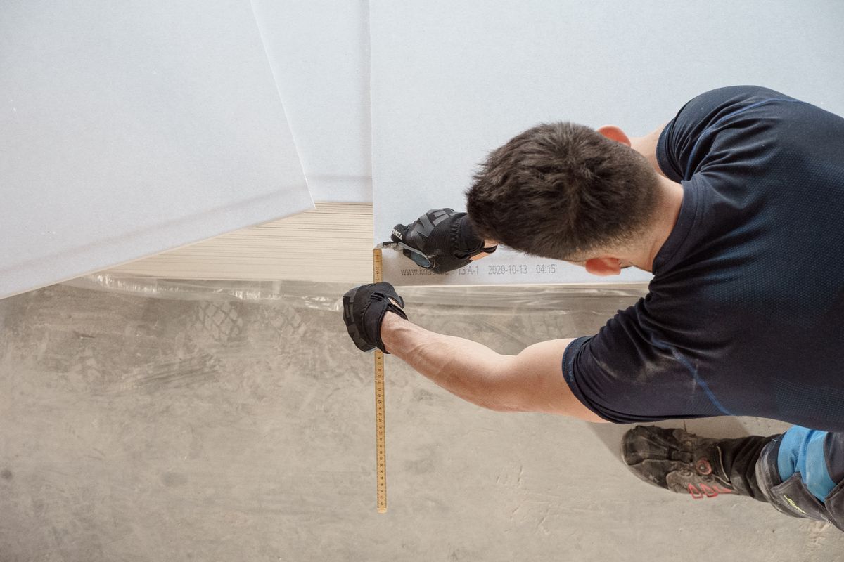 Un professionnel mesure un angle de pièce au niveau du sol avec un mètre pliant.