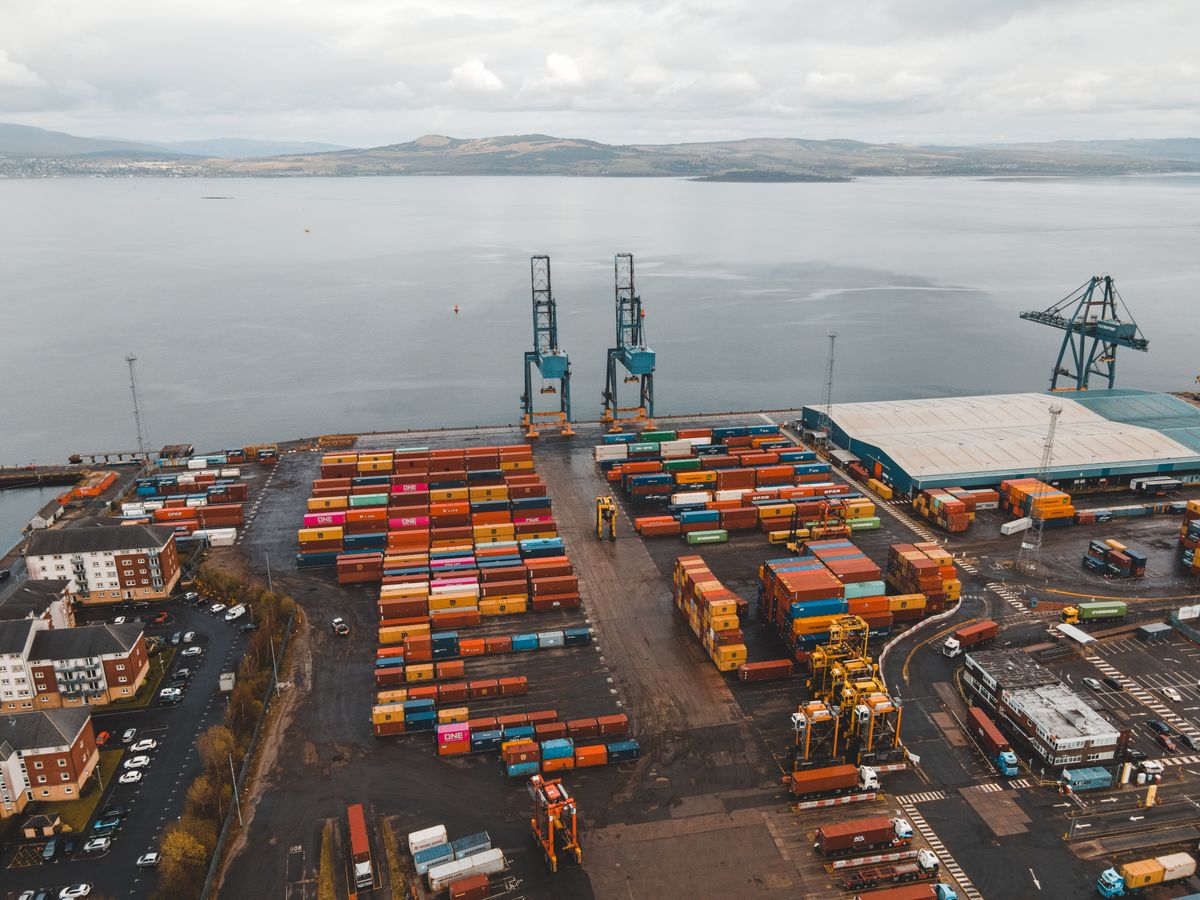 Aerial view of shipping containers in a coastal cargo terminal.