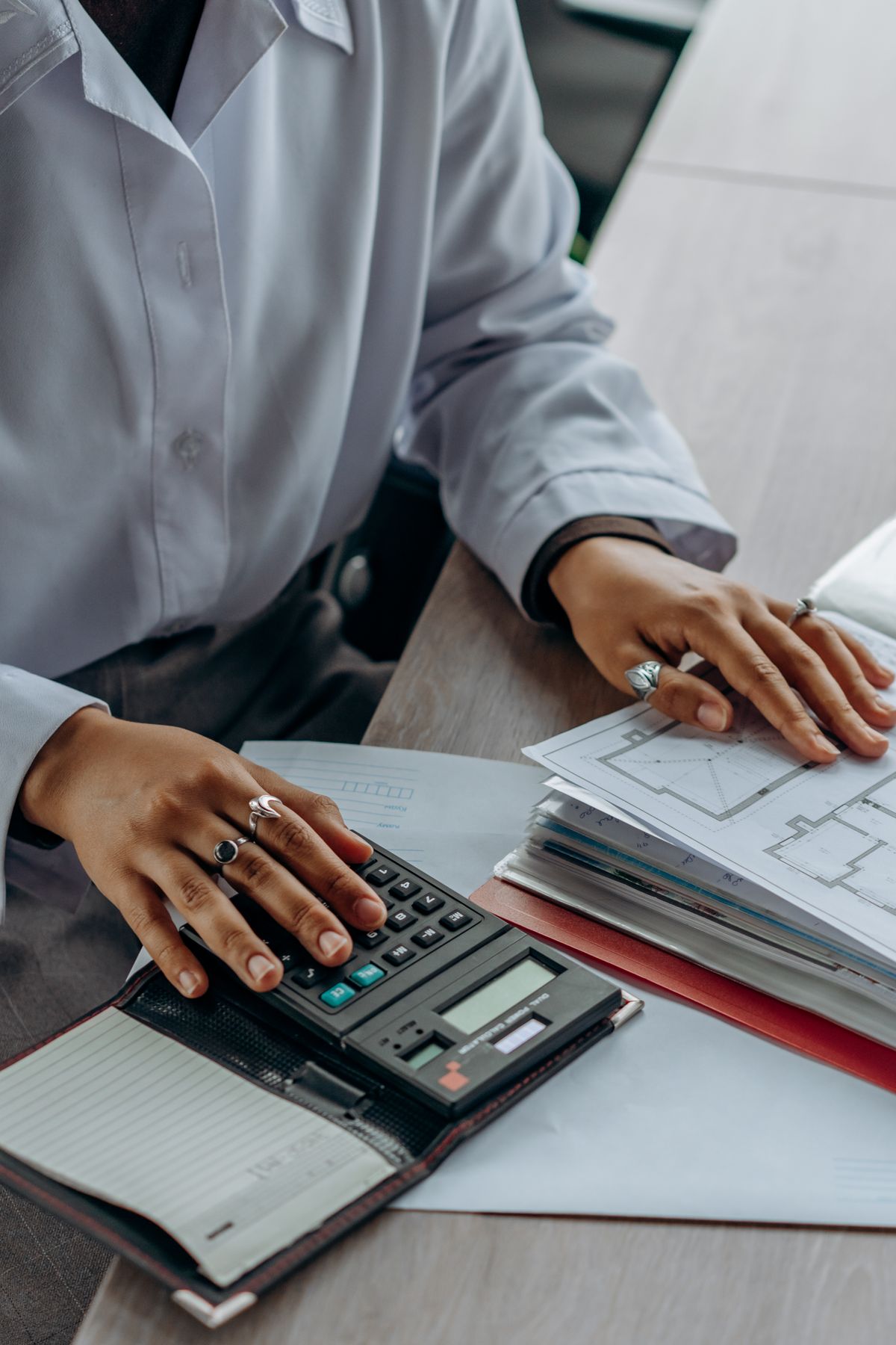 A person uses a calculator beside plans and documents on a desk.