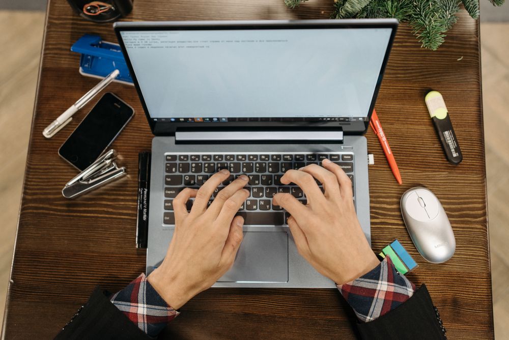 Dłonie piszące na klawiaturze laptopa stojącego na biurku.