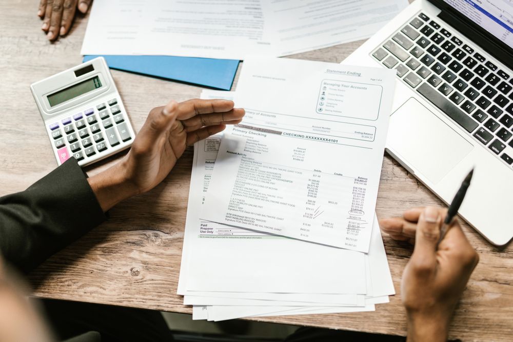 Des mains examinent des documents financiers près d’une calculatrice et d’un ordinateur.