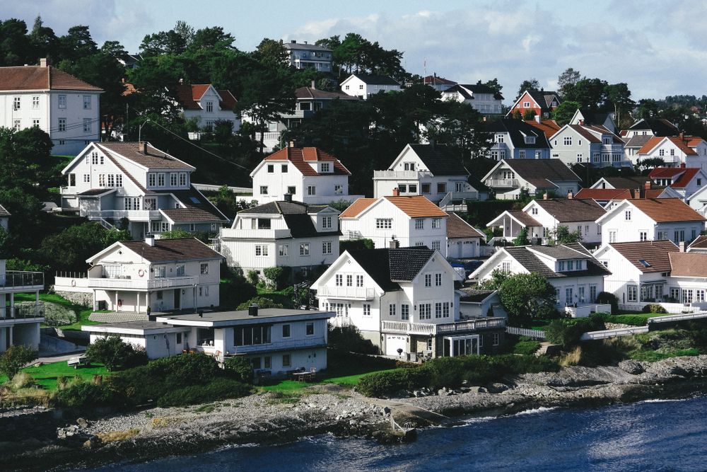Hvite bolighus ligger i en skråning langs en steinete sjøkant.