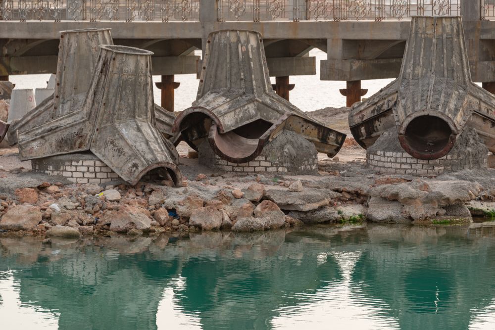 Elementos de cofragem junto à água e a uma ponte em construção.
